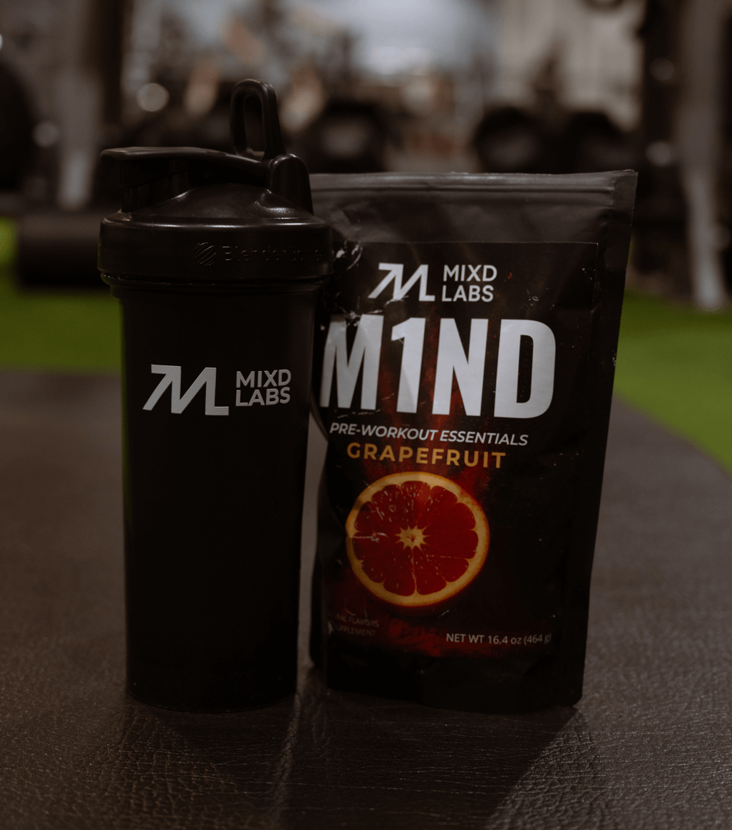 Black shaker bottle and 'M1ND' pre-workout supplement package with grapefruit flavor on a blurred background.